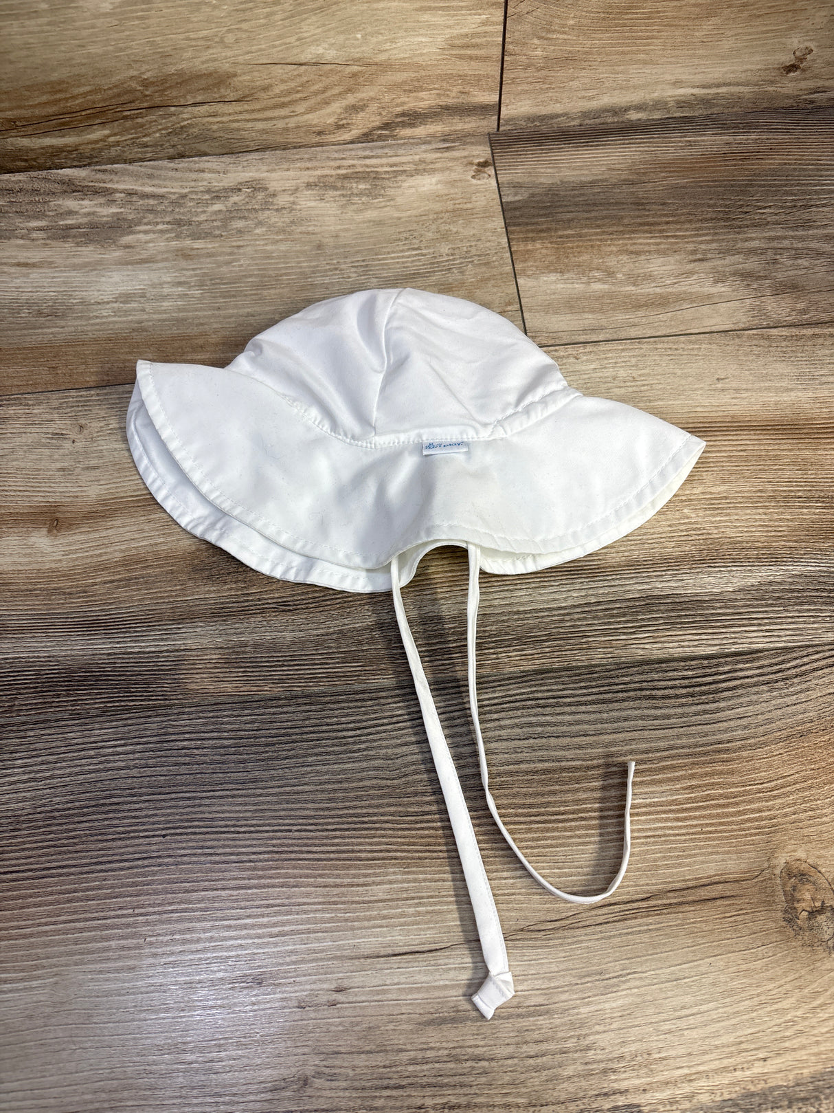 Top-down view of white iPlay by Green Sprouts swim bucket hat showing wide brim and chin ties on wood background