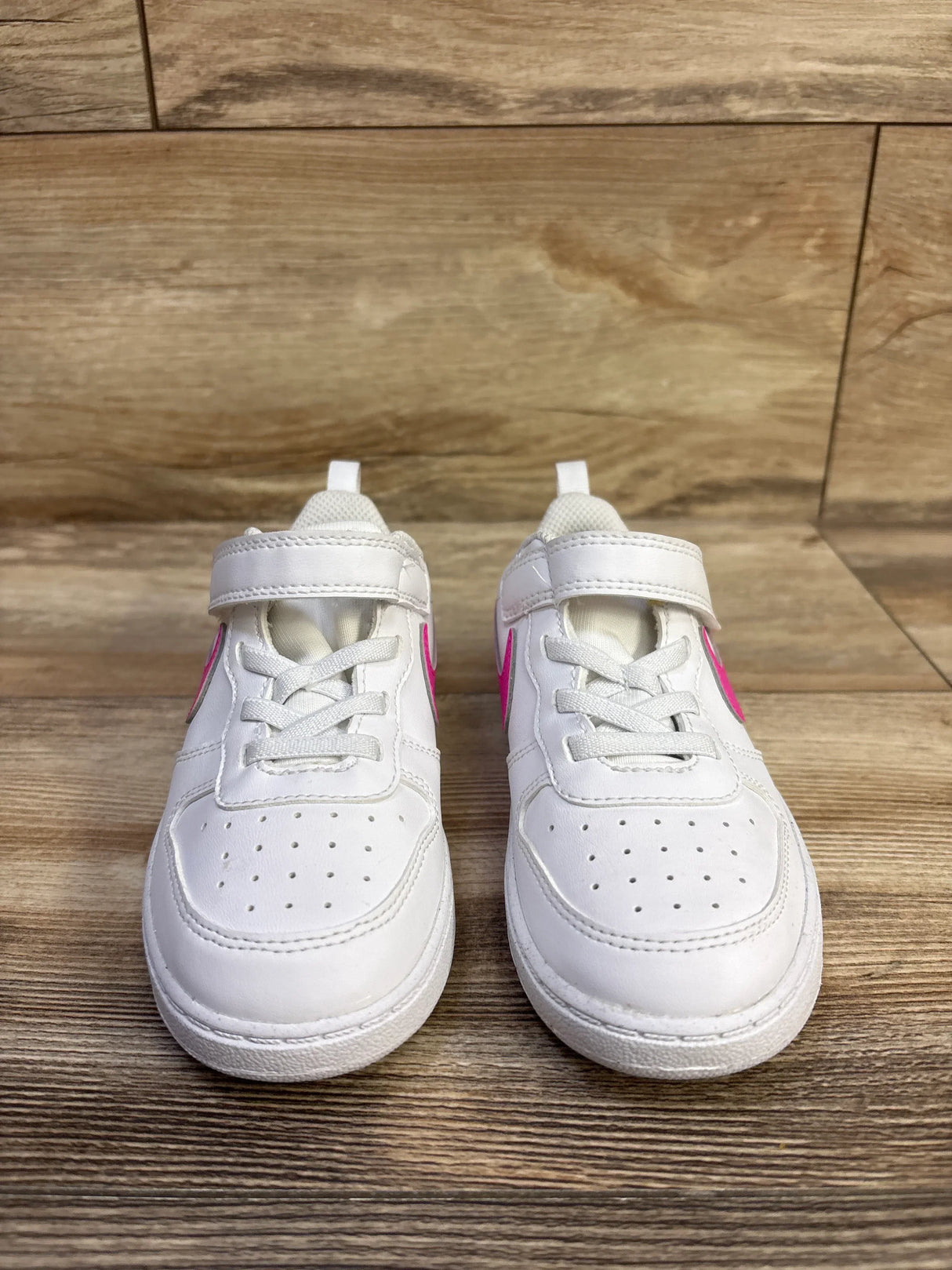 Front view of toddler Nike Court Borough sneakers size 10C showing white leather with pink Swoosh and Velcro strap on wood floor