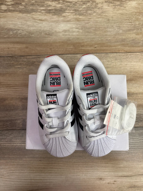 Top view of Run DMC and Adidas Superstar 50th Anniversary sneakers, white with black stripes, extra laces, box on wood