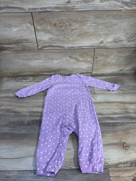 Front flat-lay of purple Care Bears coverall showcasing white heart print, long sleeves, and leg snap closures on wood floor background