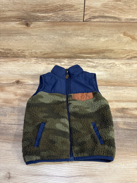 Front flat lay of Carter’s sherpa vest size 2T showing navy yoke, olive camo sherpa body, faux-leather chest patch and welt pockets on wood