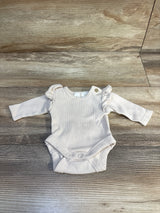 Front view of beige ribbed preemie bodysuit showcasing ruffled shoulder detail and snap crotch on light wood background