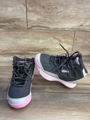 Pair of black and pink AND1 brand athletic sneakers on wooden floor and wall background