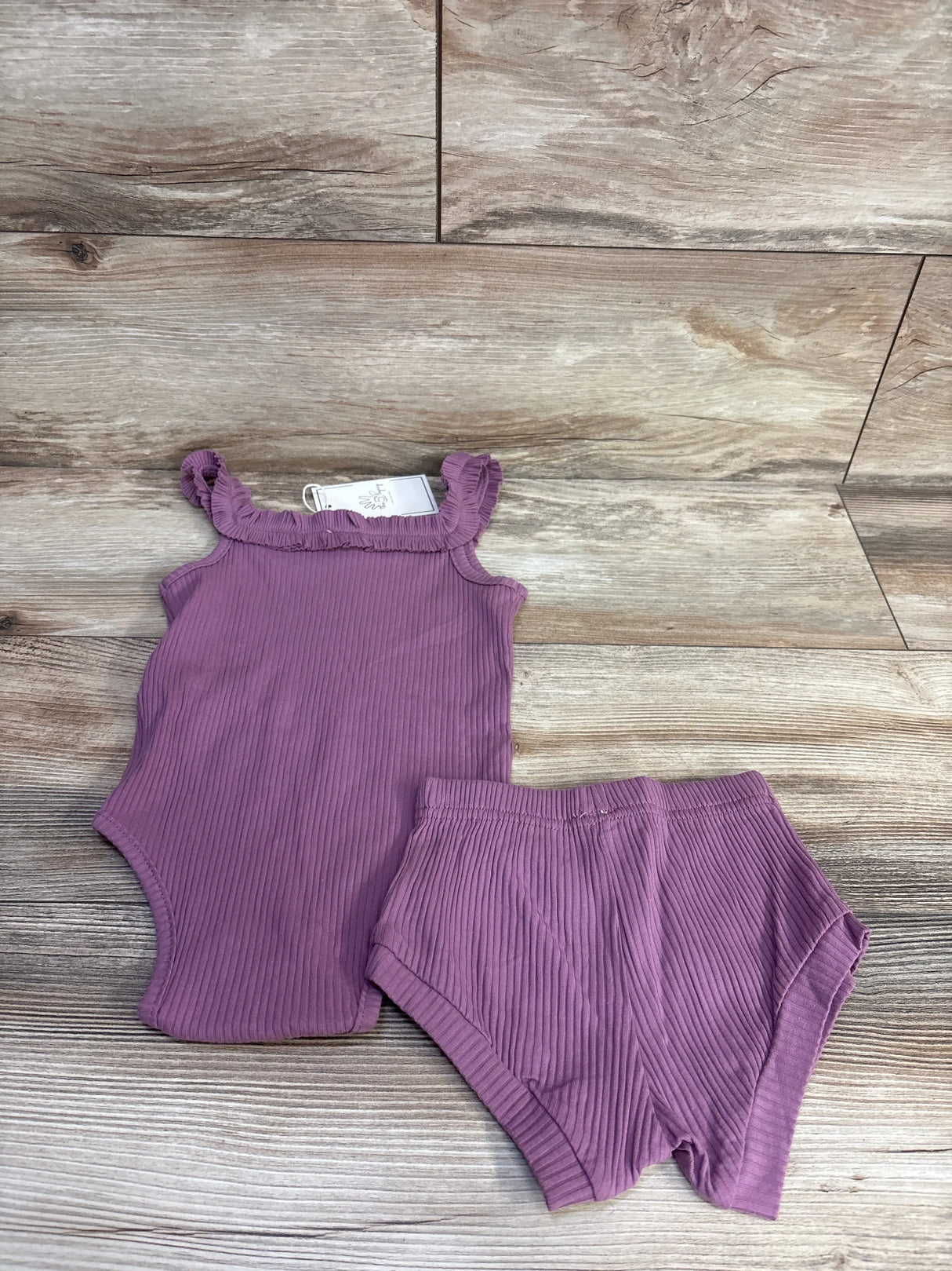 Flat lay of purple ribbed 2-piece baby tank bodysuit and shorts showing ruffle straps on wood background