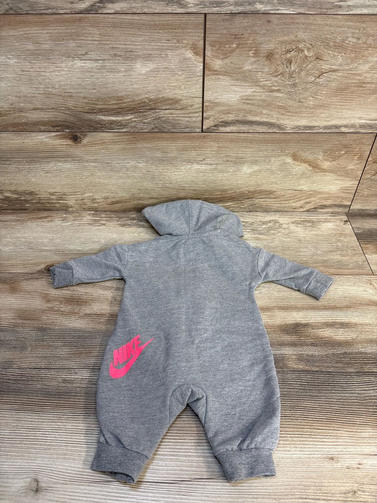 Gray baby hooded jumpsuit with pink Nike logo on wood background