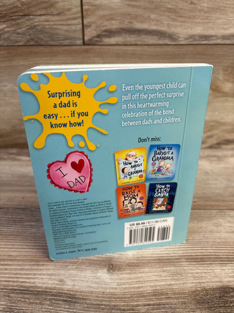 Back of How to Surprise a Dad board book with yellow splash reading Surprising a dad is easy on wood