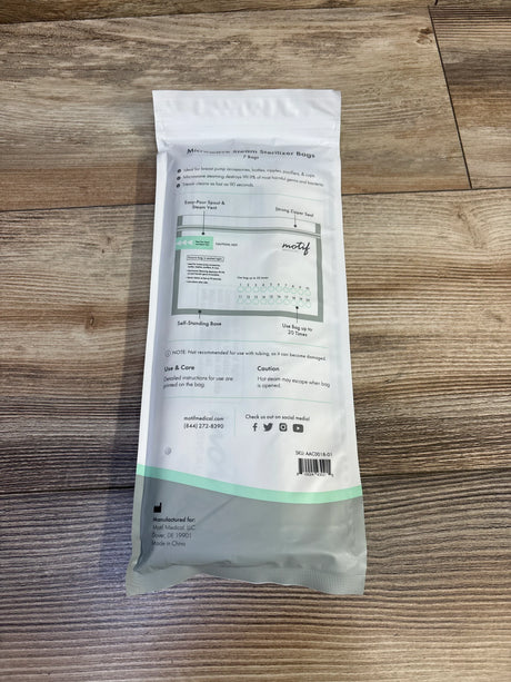 Top-down view of Motif microwave steam sterilizer bag (7-pack) showing back label with zipper-seal, pour spout diagram and usage markings on wood floor
