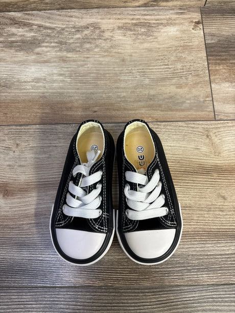 Top-down view of black low-top canvas toddler sneakers with white toe caps and laces, size 5C on wood floor