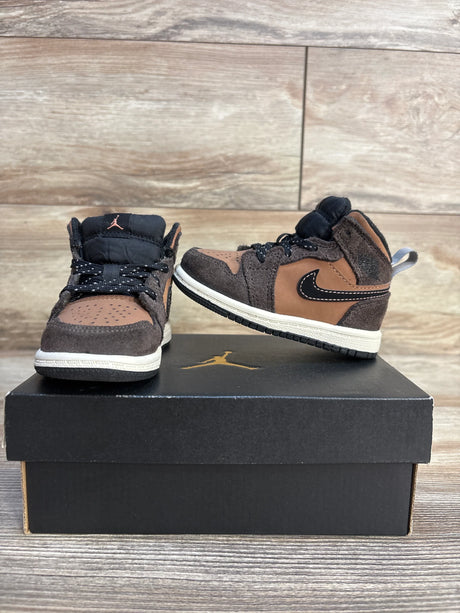 Brown and black toddler Nike high-top sneakers with white soles on a shoebox, wooden background