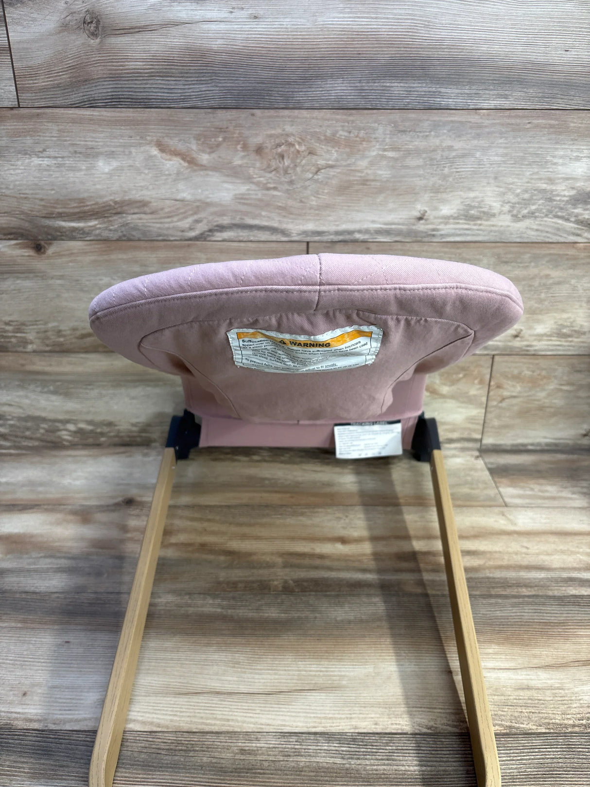 Rear view of ANGELBLISS portable baby bouncer in pink showcasing padded backrest and wooden rocker style legs on wood floor