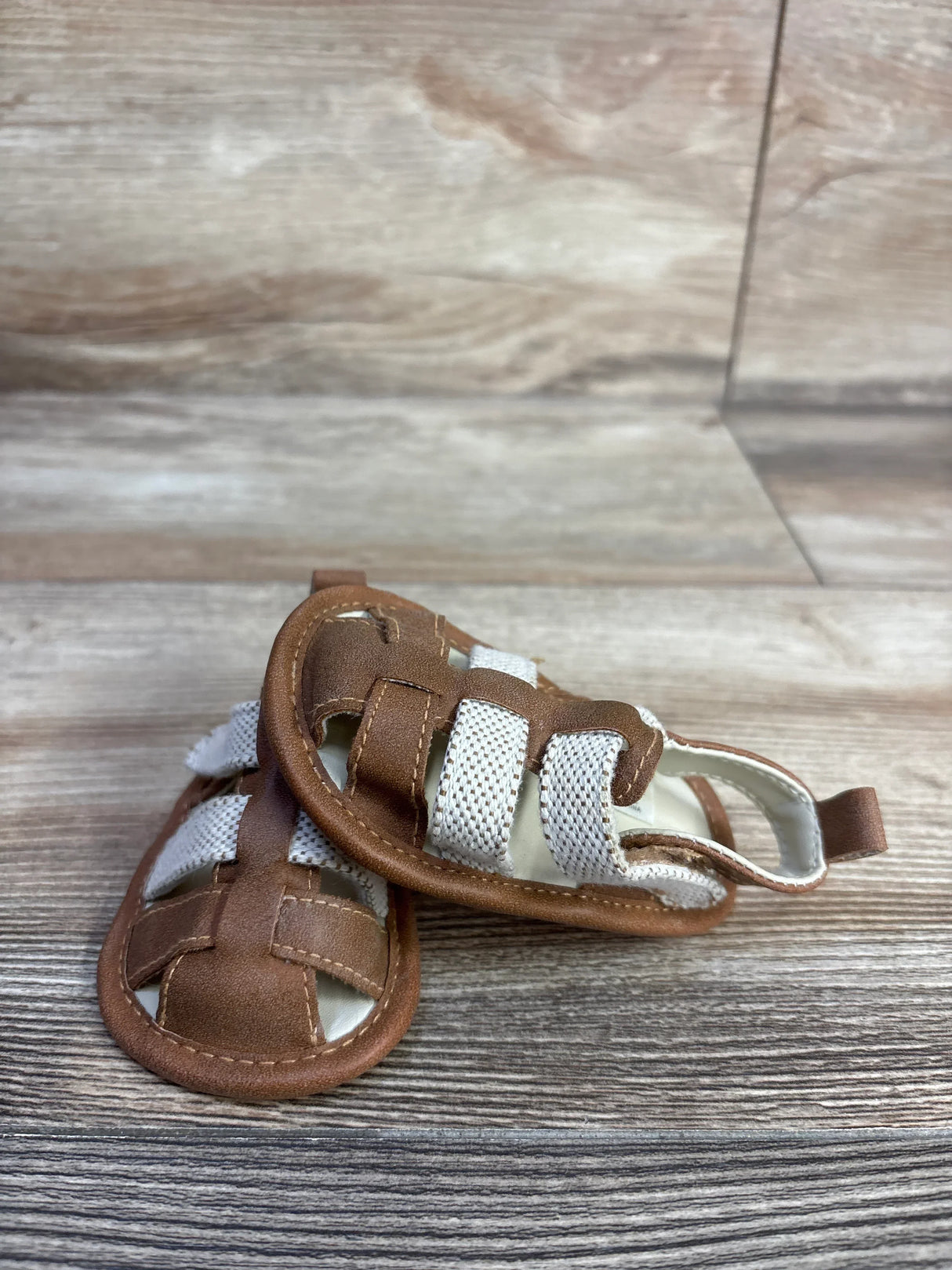 Front view of Cat and Jack tan baby sandals size 3C showing white elastic straps and stitched faux leather upper on wood