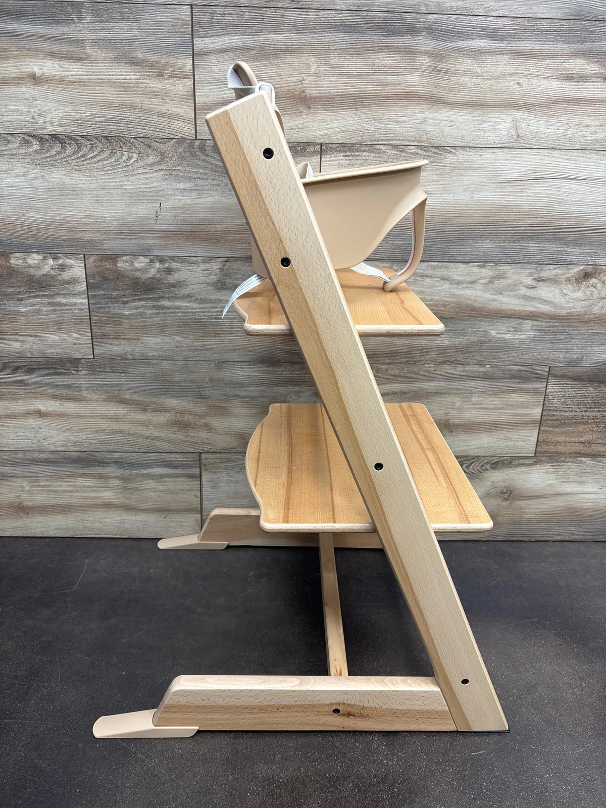 Side view of Stokke Tripp Trapp high chair with tray showcasing wooden footrests against a wood plank background