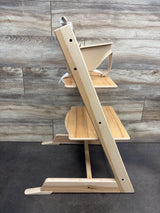 Side view of Stokke Tripp Trapp high chair with tray showcasing wooden footrests against a wood plank background