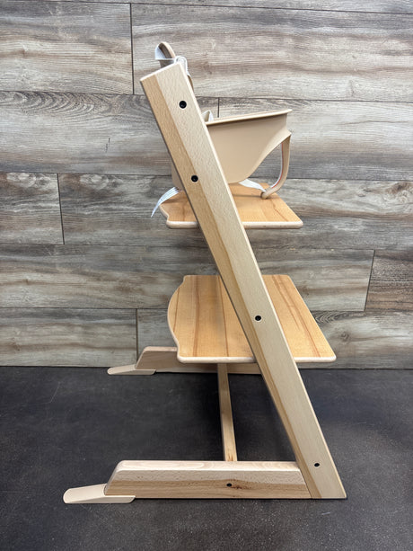 Side view of Stokke Tripp Trapp high chair with tray showcasing wooden footrests against a wood plank background