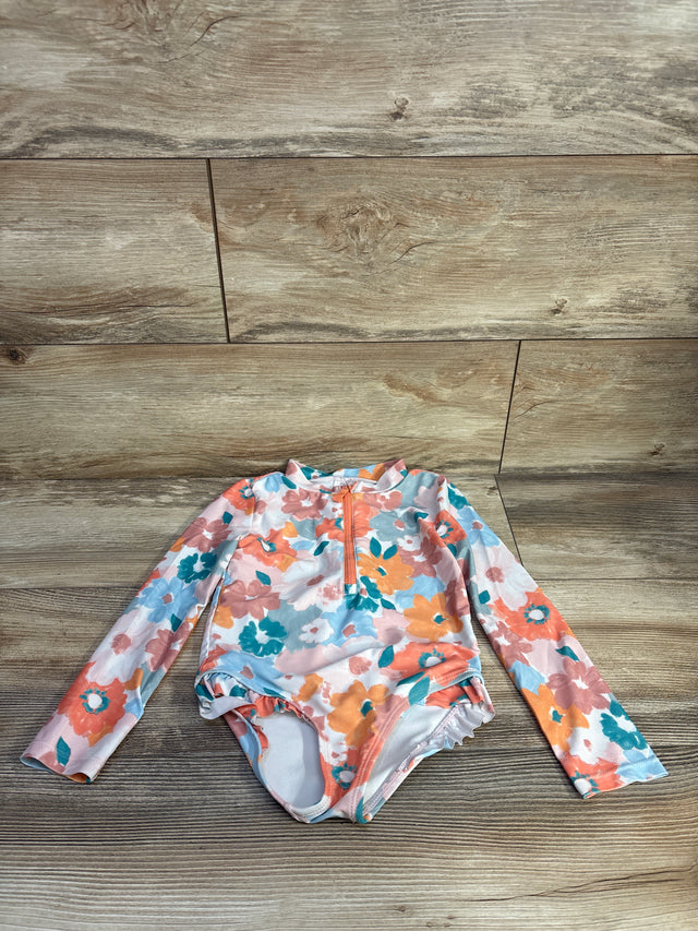 Flat lay of toddler long-sleeve floral rashguard one-piece swimsuit with front zipper and ruffle leg trim on wood background