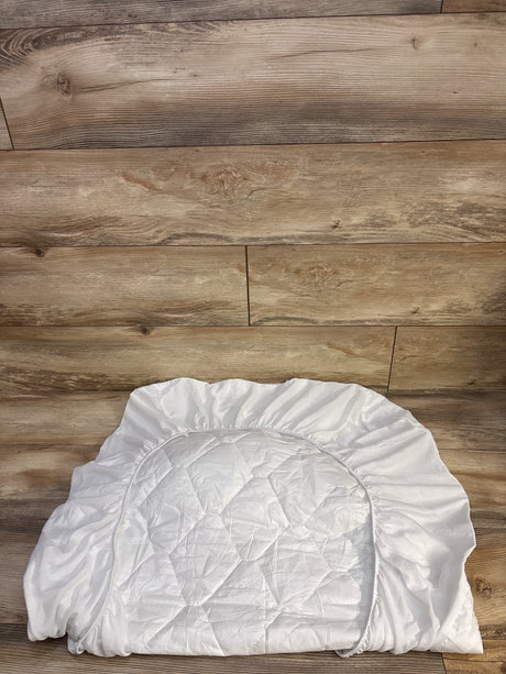 Top view of Amfori crib mattress protector showing quilted waterproof center and elastic fitted skirt on wood floor