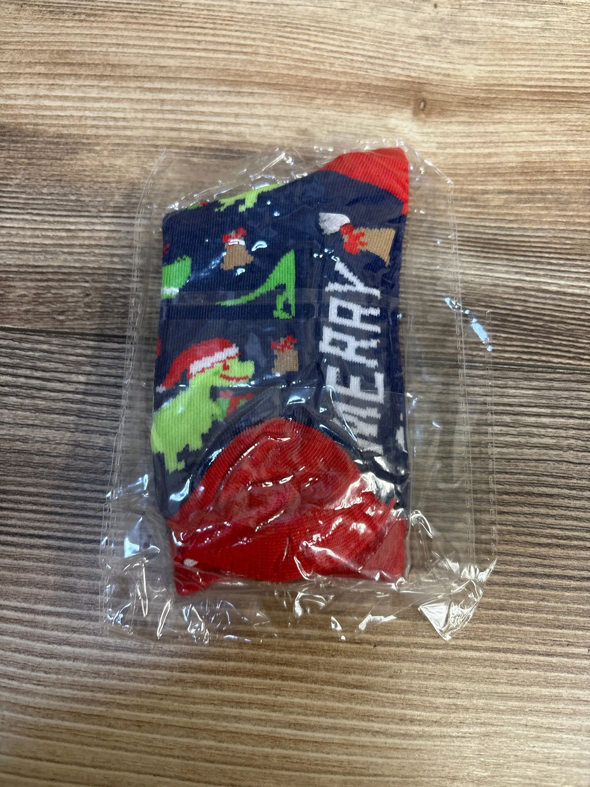 Kids' Christmas dinosaur socks with festive print, red cuffs, packaged for resale