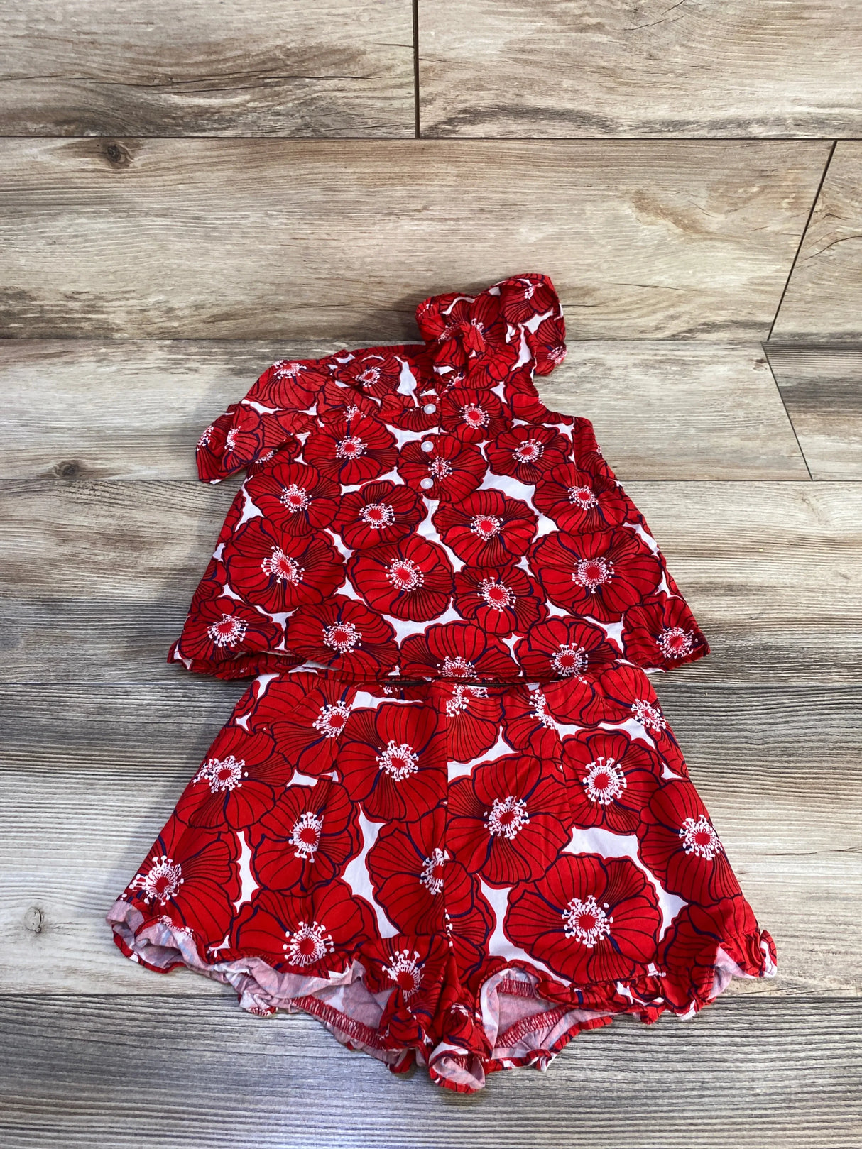 Top-down of Janie and Jack red poppy sun top and ruffle-hem shorts, one-shoulder ruffle, light wood background