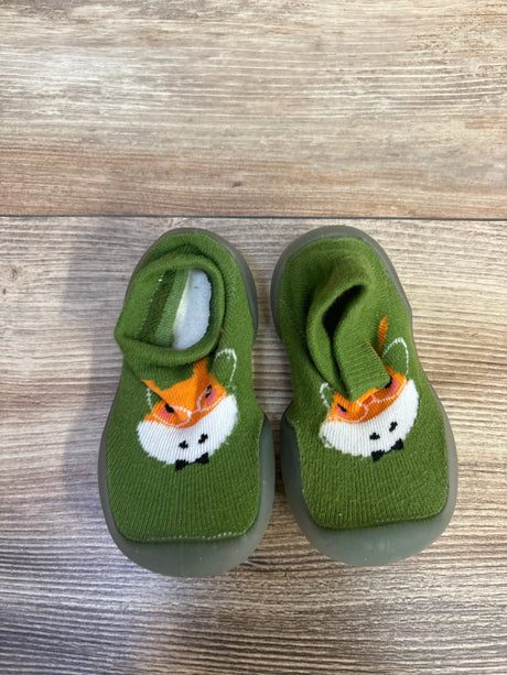 Top-down view of Ikevan green knitted baby sock shoes showcasing orange animal-face knit and gray rubber soles on wood floor