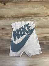 Flat lay of beige baby romper (3M) showcasing large dark gray NIKE wordmark and swoosh on a wood floor