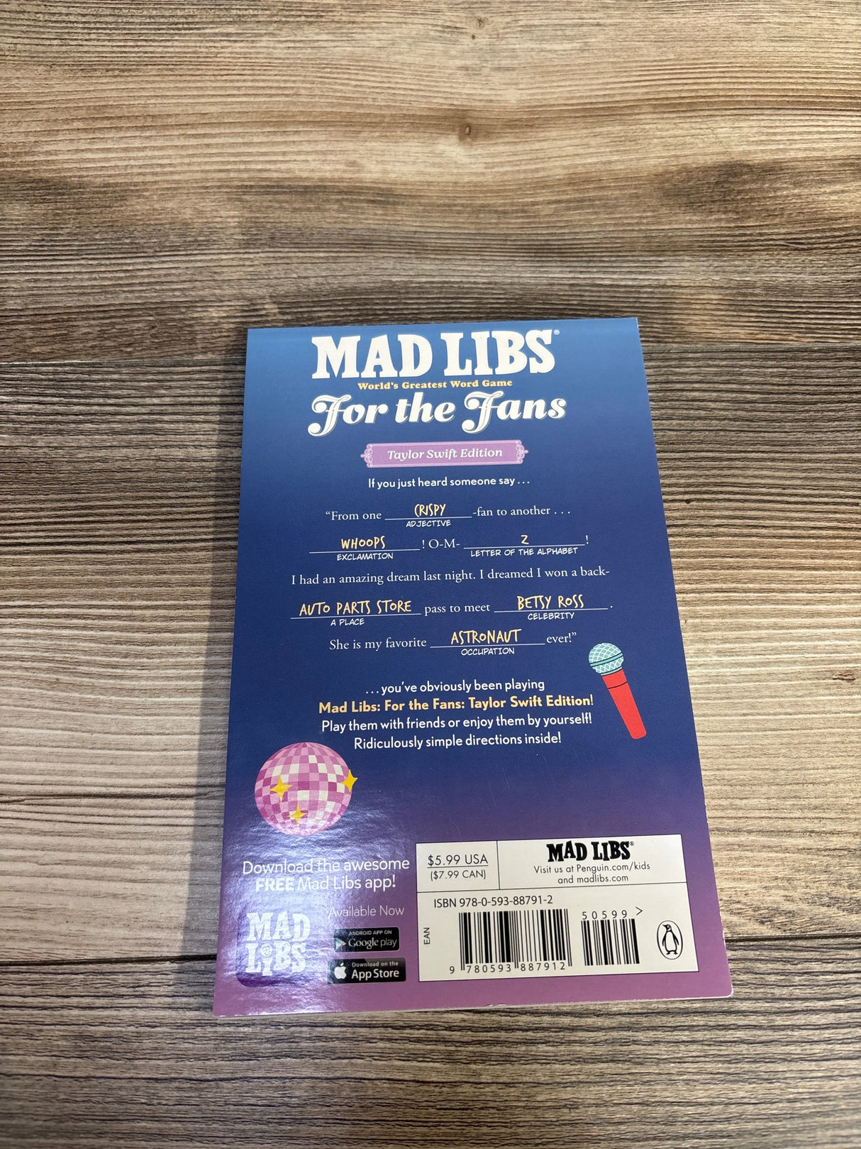 Top-down view of Mad Libs For the Fans: Taylor Swift Edition back cover showing filled-in prompts and barcode on wood table