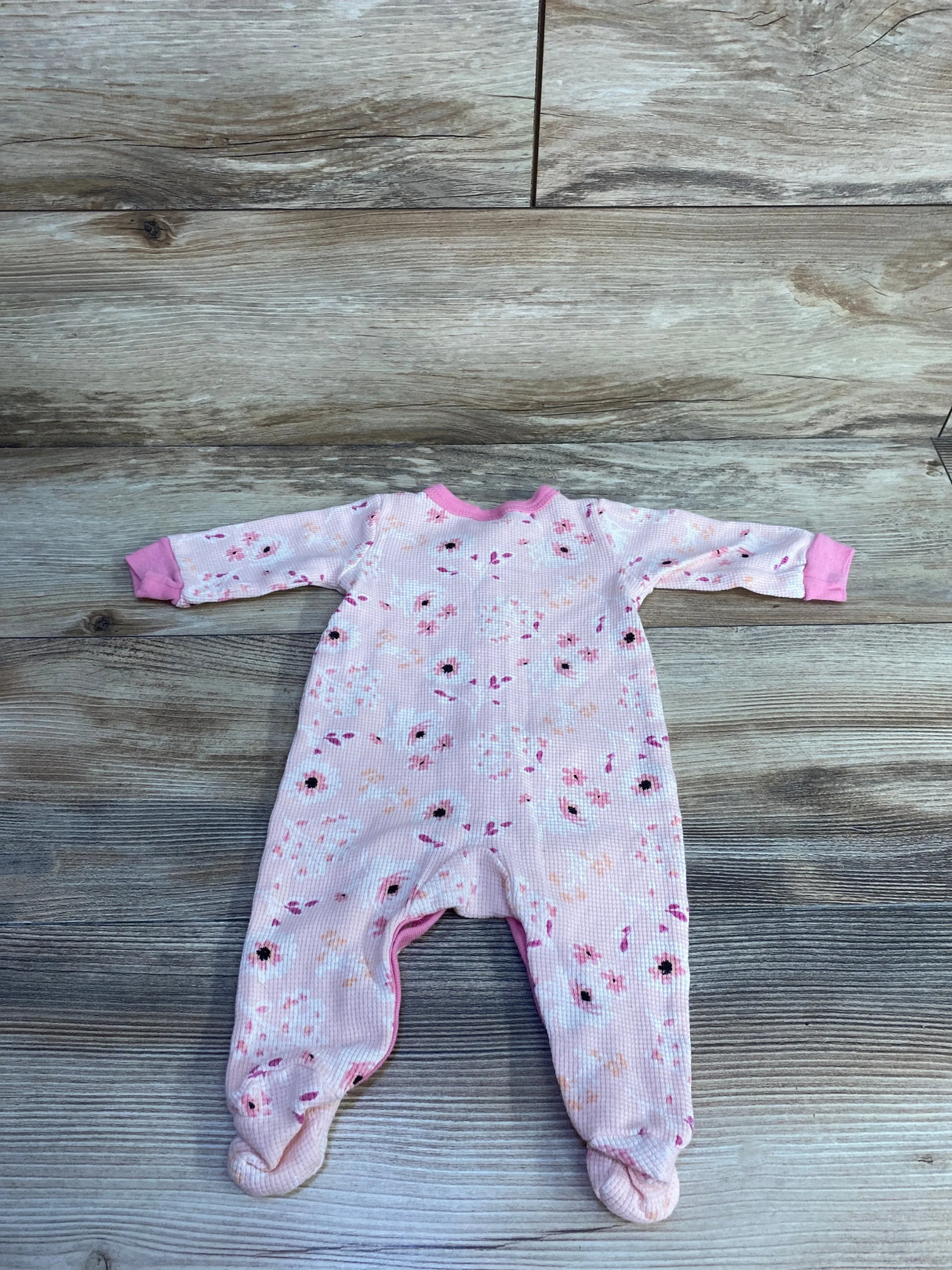 Flat lay of Little Beginnings waffle knit footed sleeper, pink floral print, size 3-6 months, on wood plank background