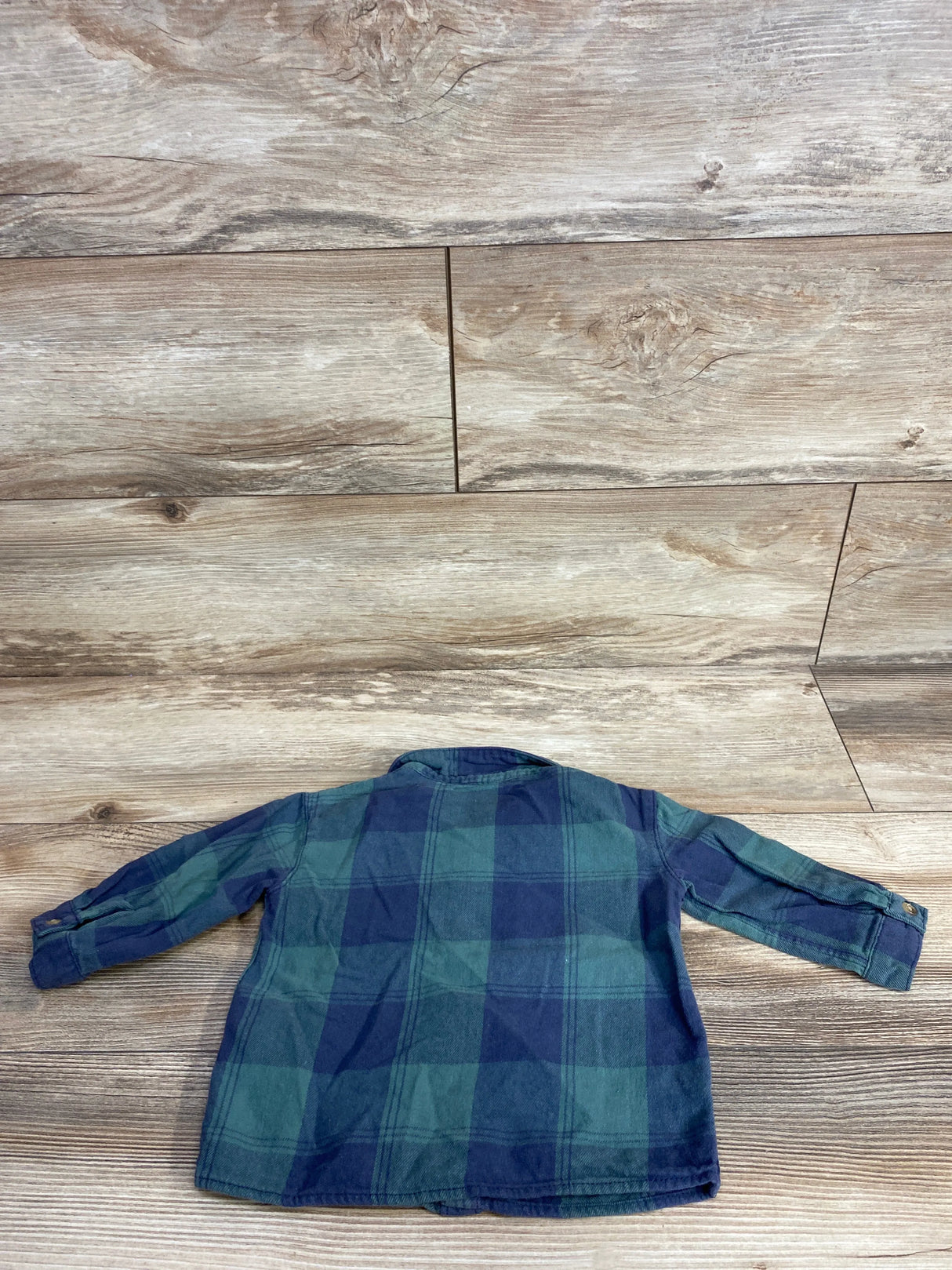 Back view of a toddler's green and navy blue plaid long sleeve shirt on wood floor
