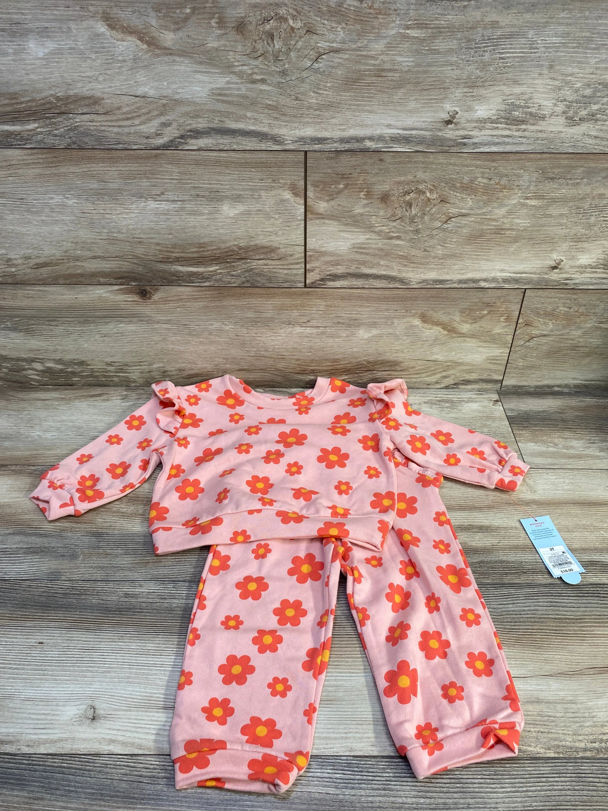 Flat lay of Cat & Jack 2T floral French terry set showing peach top with ruffle shoulders and matching pants on wood background