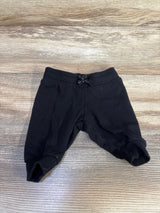 Top-down view of newborn black jogger pants showing elastic waist with tied drawstring and cuffed ankles on wood background