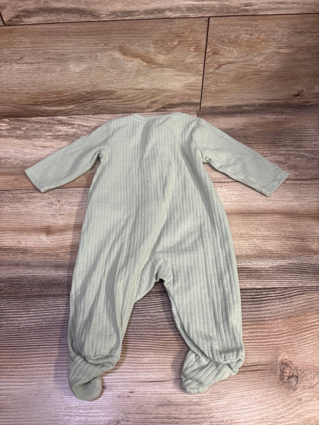 Top-down view of a green ribbed baby sleeper with long sleeves and footed legs on a wood-patterned background