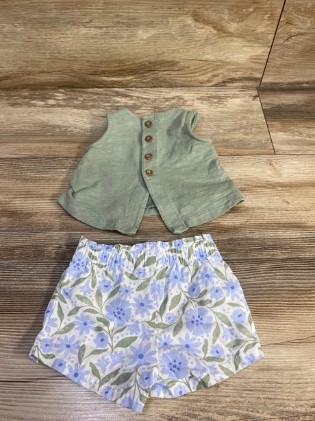 Flat lay of green sleeveless baby tank top with wooden buttons and blue floral elastic waist shorts, size 3M, on wood background