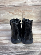 Rear view of kids' black faux leather boots showing shiny patent finish, pull tabs, and flat rubber soles on wood floor