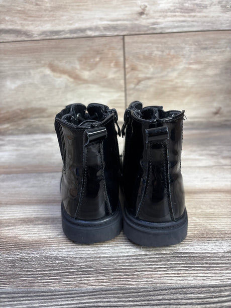 Rear view of kids' black faux leather boots showing shiny patent finish, pull tabs, and flat rubber soles on wood floor