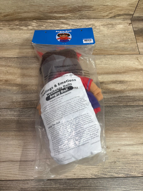 Front view of Feelings and Emotions Washable Angry Doll in clear packaging, showing red and purple clothing on a wood floor