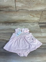 Flat lay of pink baby bodysuit dress showcasing polka dot yoke, bow, and embroidered bear applique on wood floor background
