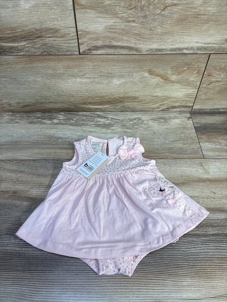 Flat lay of pink baby bodysuit dress showcasing polka dot yoke, bow, and embroidered bear applique on wood floor background