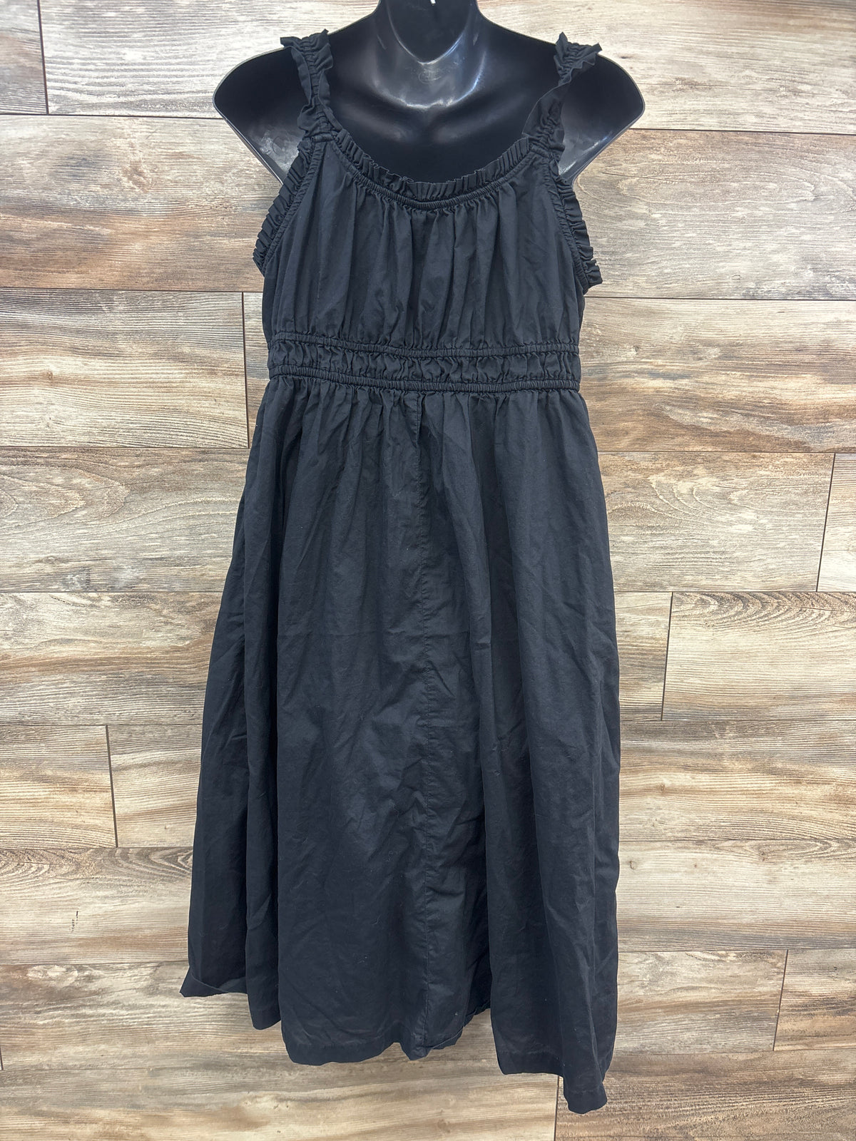 Front view of Old Navy black maternity sleeveless dress showcasing ruched straps and gathered waist on a wood-look floor