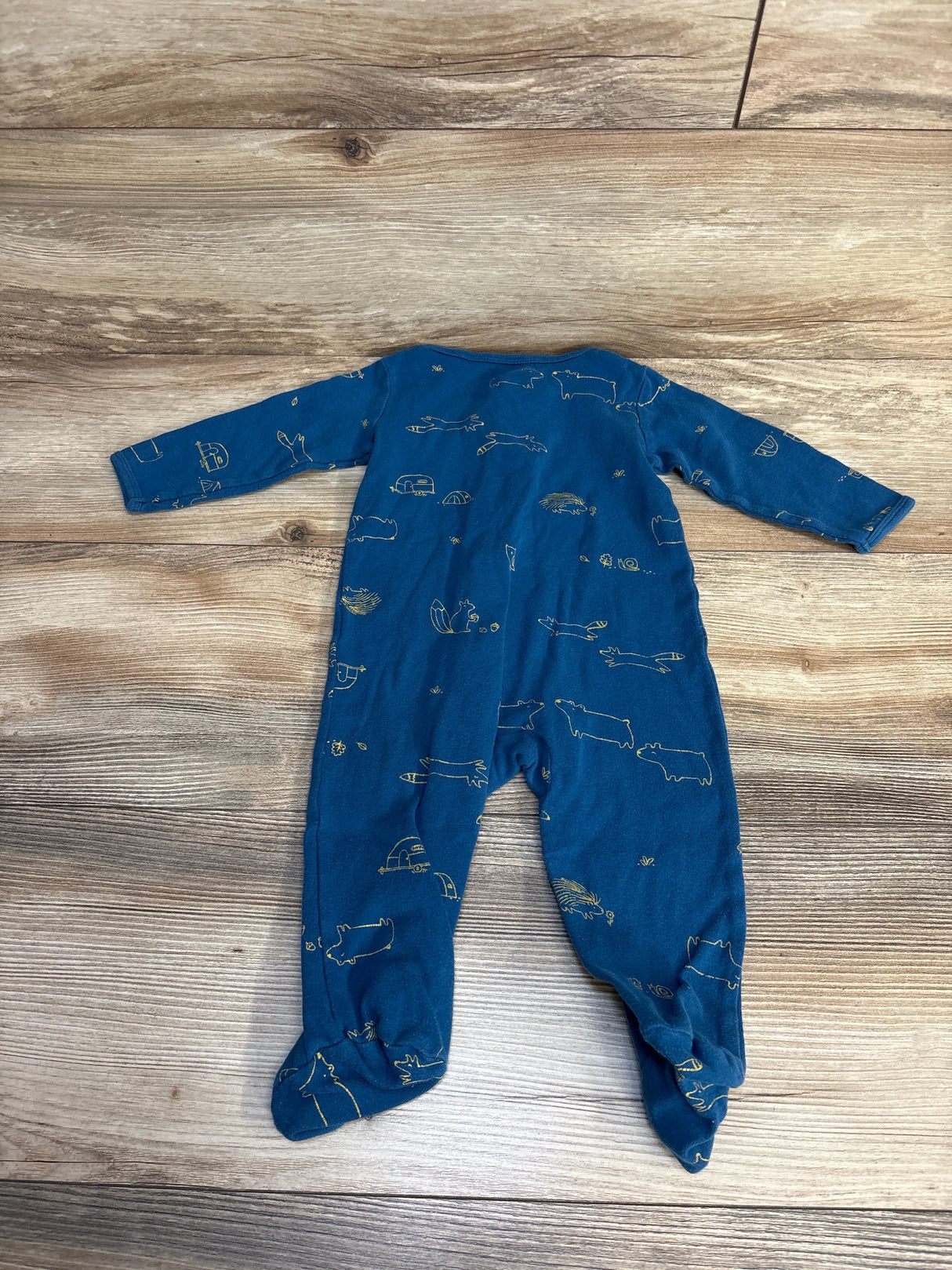 Blue baby footed pajamas with gold animal print, laid on wood floor