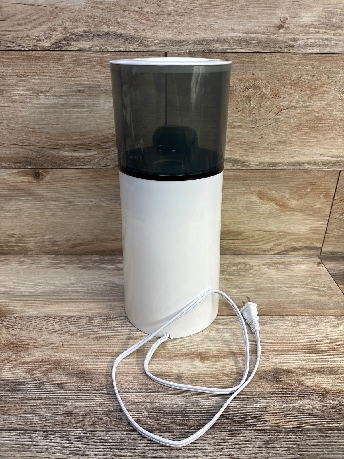 Front view of Baby Brezza Instant Bottle Warmer, White showcasing its dark translucent water reservoir and power cord on a wood surface