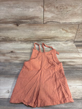 Top-down view of coral gauze shortalls showing crinkled gauze texture and knotted shoulder straps on light wood background