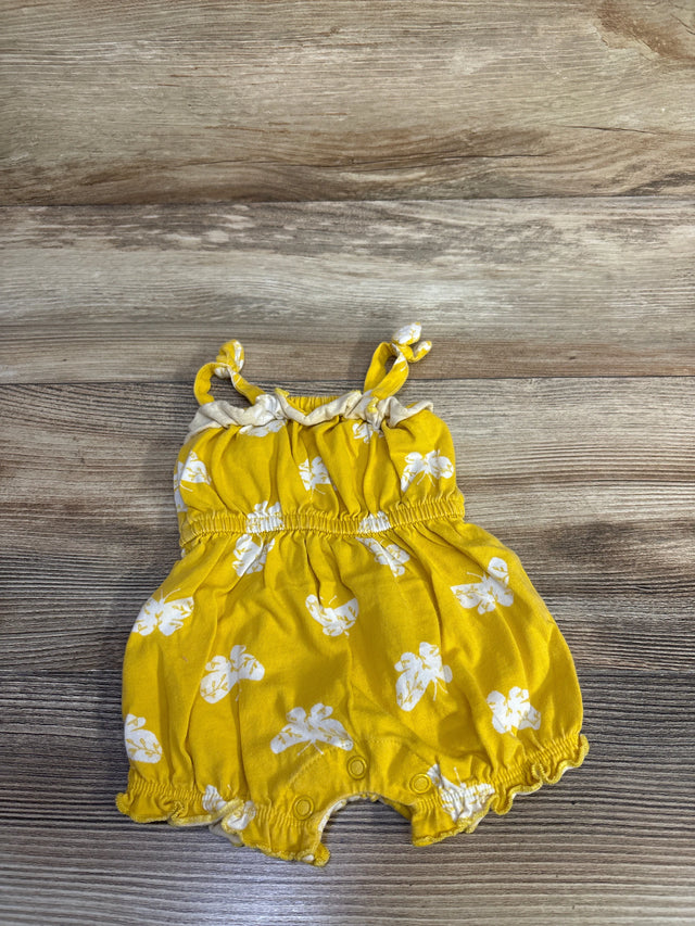 Top view of yellow baby romper with white floral print, knotted straps, elastic waist and leg cuffs, snap crotch on wood