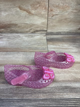 Three-quarter view of pink glitter jelly Mary Jane flats with butterfly charm and hook-and-loop strap on wood floor
