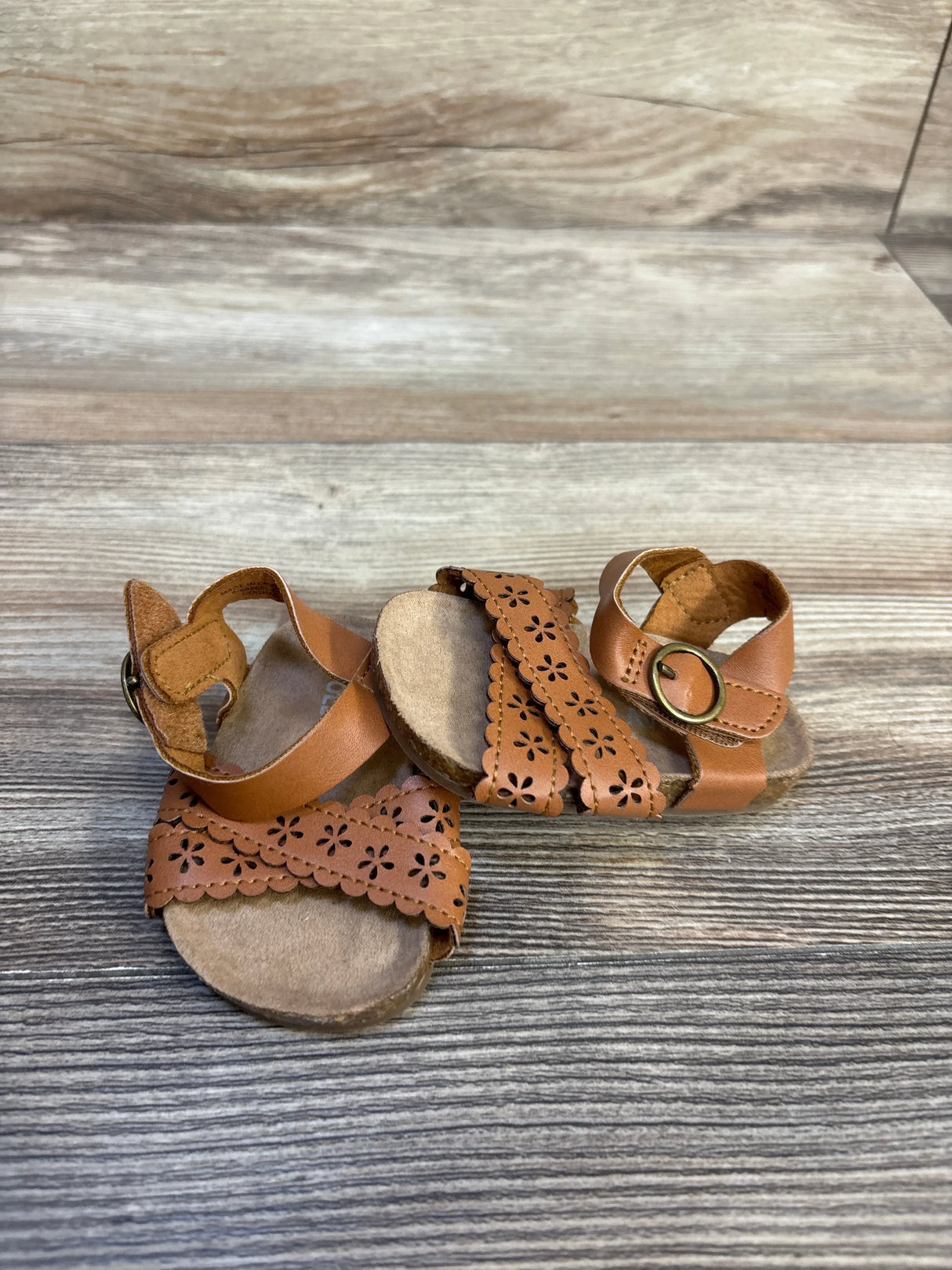 Brown toddler sandals with floral cutout straps on wood background