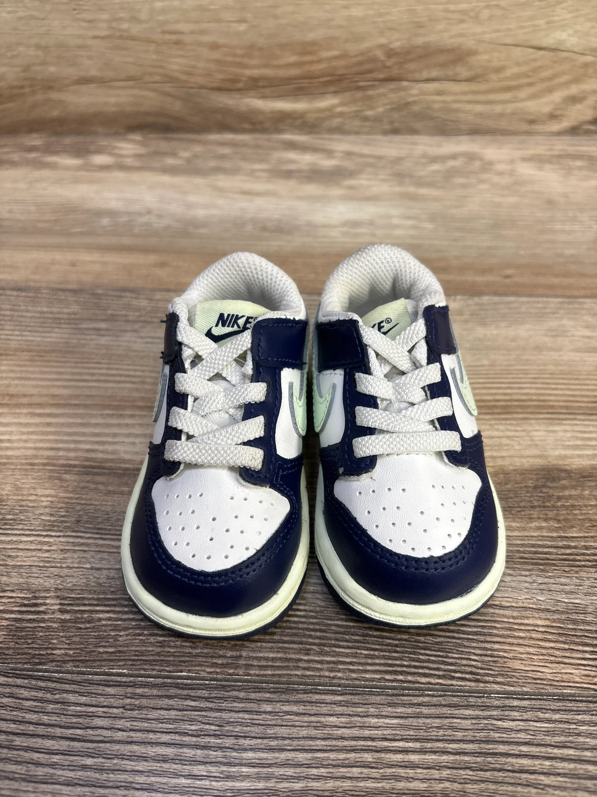 Front view of Nike Dunk Low TD sneakers in midnight navy, white, and volt tint, perforated toe and white laces on wood background