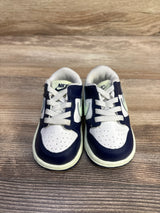 Front view of Nike Dunk Low TD sneakers in midnight navy, white, and volt tint, perforated toe and white laces on wood background