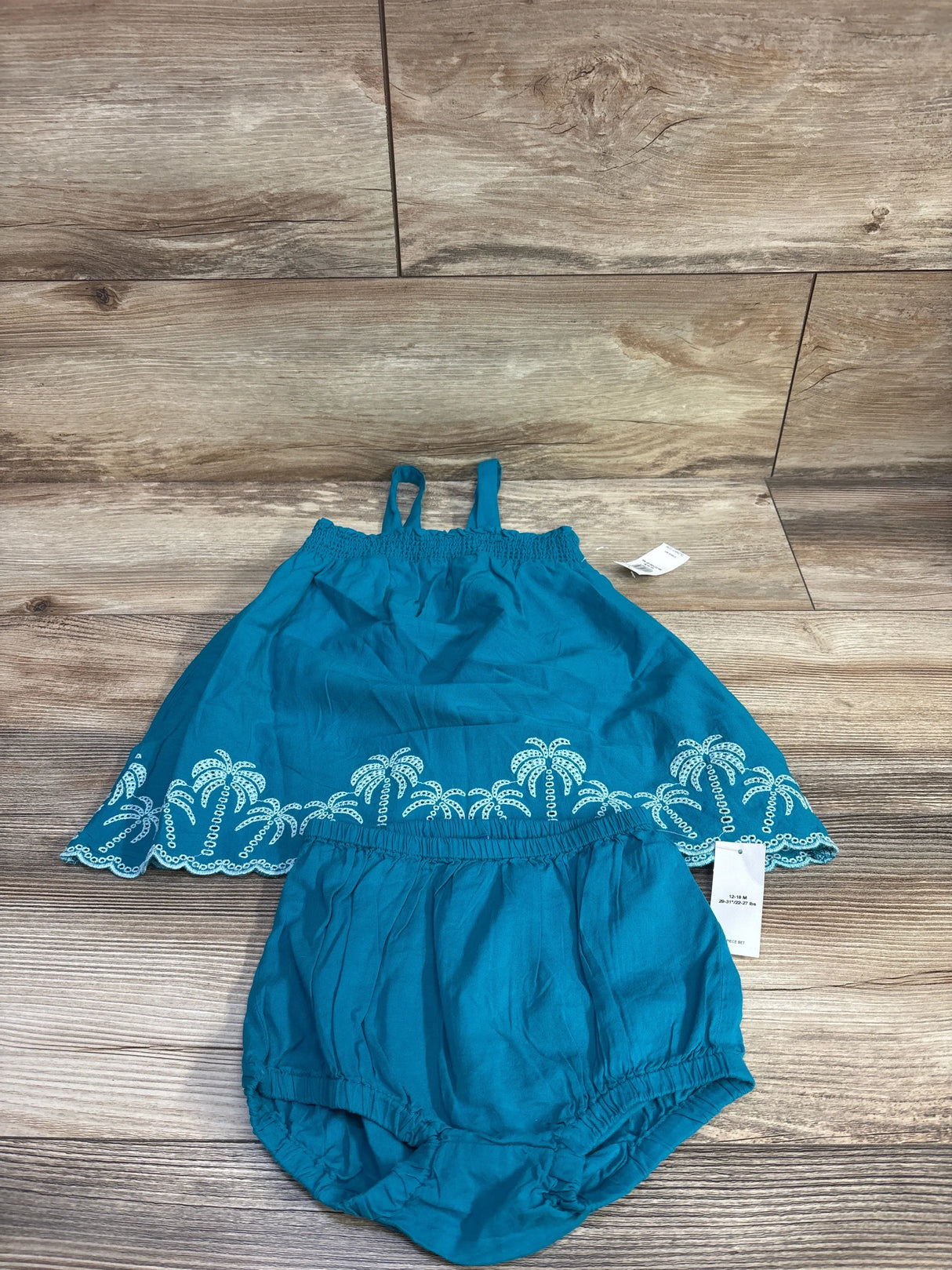 Top view of teal Old Navy baby two-piece smocked embroidered tank top and bloomer shorts showcasing scalloped embroidered hem on wood background