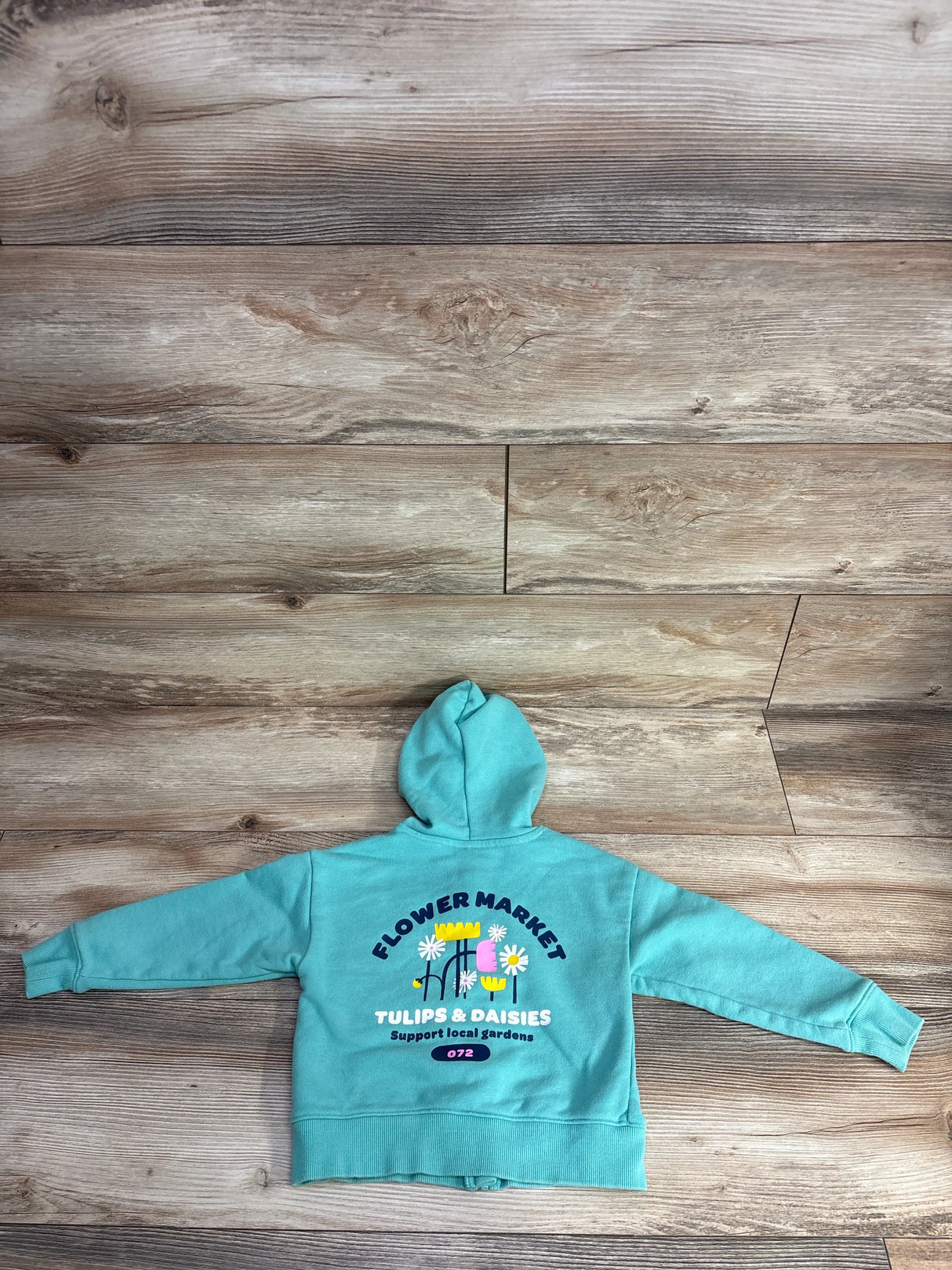 Turquoise children's hoodie with colorful flower market print and text Tulips & Daisies on wood floor