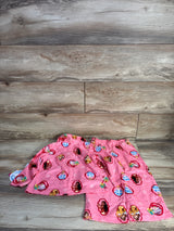 Flat lay of pink Disney Princess 2-piece pajama set, button-up top and elastic-waist pants with princess print on wood
