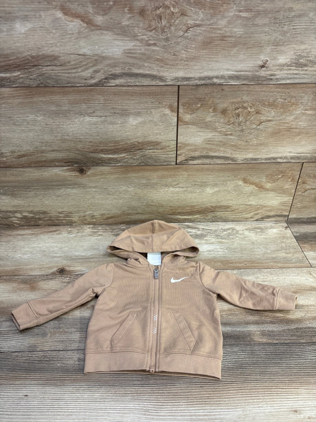 Front view of Nike tan zip up hoodie, size 6 months, with hood, pockets, and swoosh logo on wood