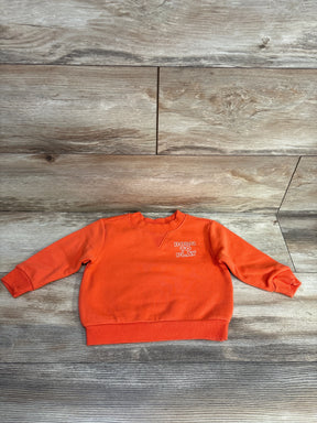 Orange toddler sweatshirt with "Born to Play" text on chest, laid flat on wooden floor background